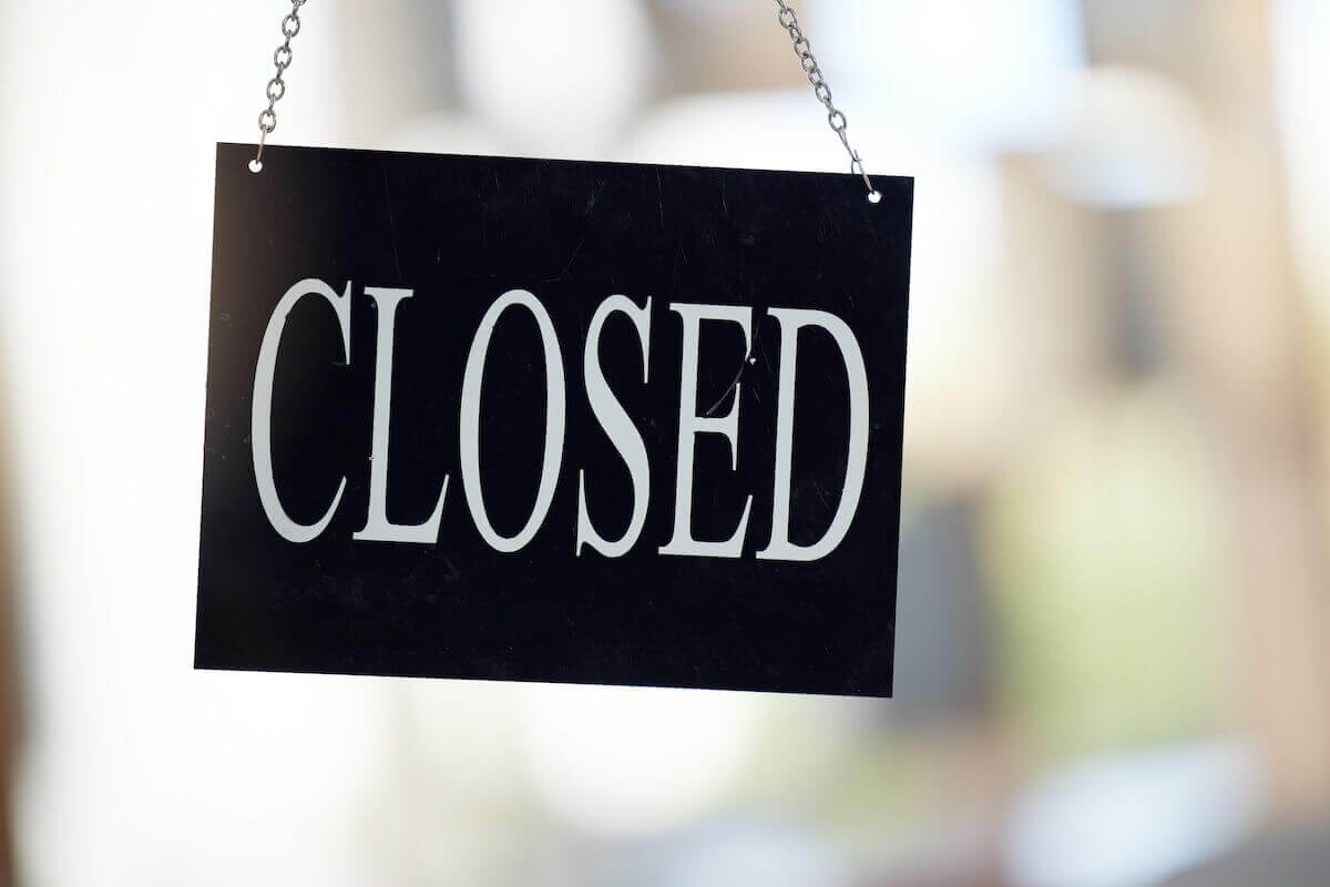 Black closed sign with white letters hanging in a window