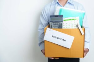 Employee holding a box of items from his desk with an envelope labeled 'resignation' taped to the front of it