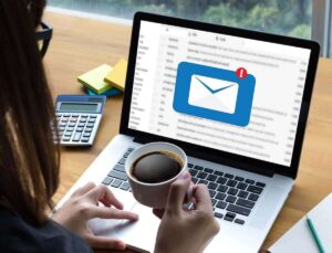 An employee holds a coffee cup while working on a laptop. A new email icon is pictured in the middle of the screen