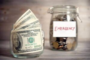 Jar of cash in the foreground and a jar of coins in the background labeled 'emergency'