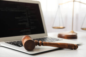 Wooden judge's gavel on a laptop keyboard with justice scales in the background