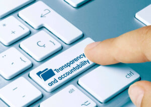 Close up of a person's finger pressing a key on a keyboard labeled 'transparency and accountability'