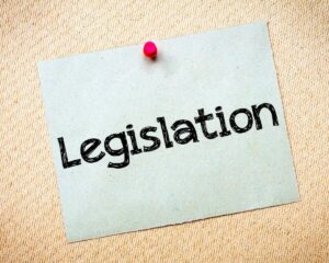 Sticky note attached to a wall with a red push pin that says 'legislation'