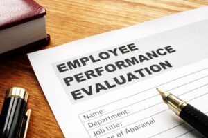 Close up of the top of a form on a desk titled "employee performance evaluation' with a pen on top of it; a pen and book are off to the side of it