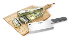 Pile of cut up money on a cutting board with a meat cleaver next to it