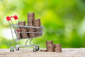 Small shopping cart filled with stacks of coins against a green foliage background