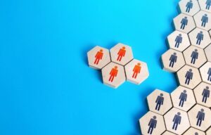 Four wooden blocks with red person icons on them separated from a larger group of wooden blocks with black person icons against a solid light blue background