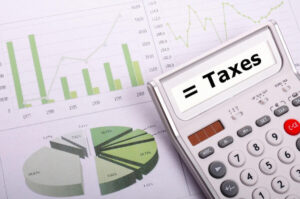 Calculator sitting on top of printed financial graphs with the word 'taxes' on its screen