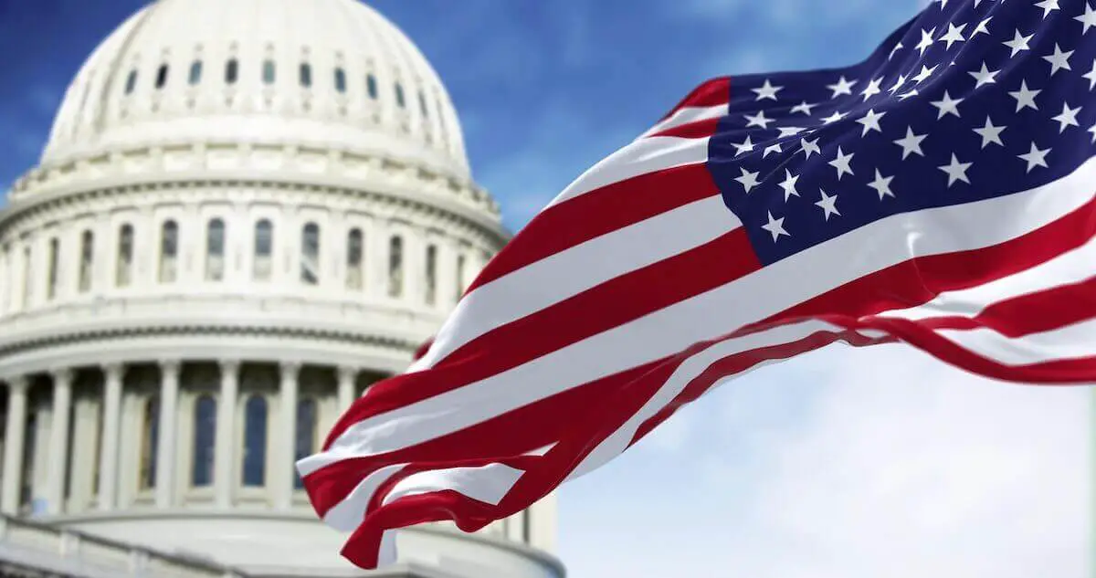 USA flag flying in the wind with the U.S. Capitol building pictured behind it against a blue sky