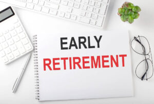 index card that reads 'early retirement' on a desk surrounded by reading glasses, a keyboard, and calculator
