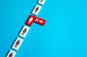 Row of black and white person icon blocks in a vertical row with a red and white person icon in the middle with an 'X' and a right arrow on it depicting RIFs, job cuts or workforce layoffs