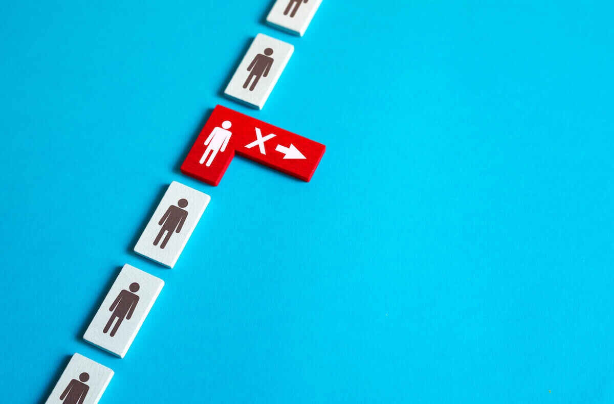 Row of black and white person icon blocks in a vertical row with a red and white person icon in the middle with an 'X' and a right arrow on it depicting RIFs, job cuts or workforce layoffs