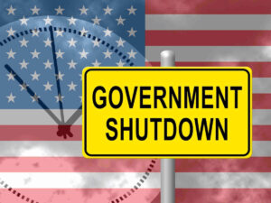 Yellow sign reading 'government shutdown' overlaid on an American flag with a silhouette of a ticking clock