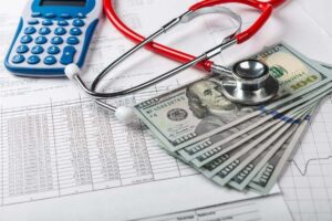 Spread of cash on top of documents along with a calculator and stethoscope