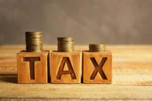 wooden blocks spelling the word 'tax' with vertical stacks of coins on top of each decreasing in size from right to left
