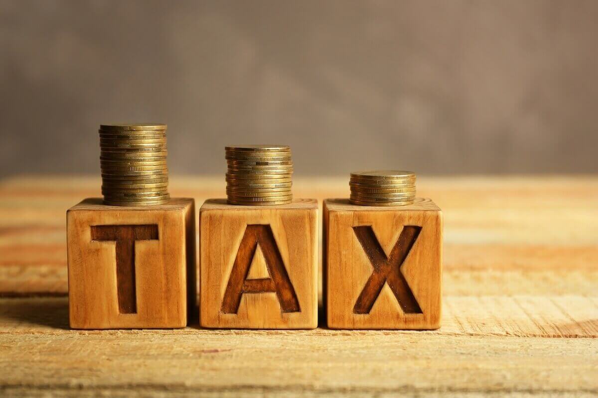 wooden blocks spelling the word 'tax' with vertical stacks of coins on top of each decreasing in size from right to left