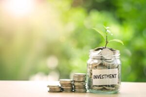 Vertical stacks of coins growing in size next to a glass jar with a green plant growing out of the top labeled 'investment'