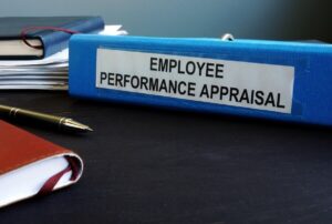 Binder labeled 'employee performance appraisal' on a desk next to a pen and books