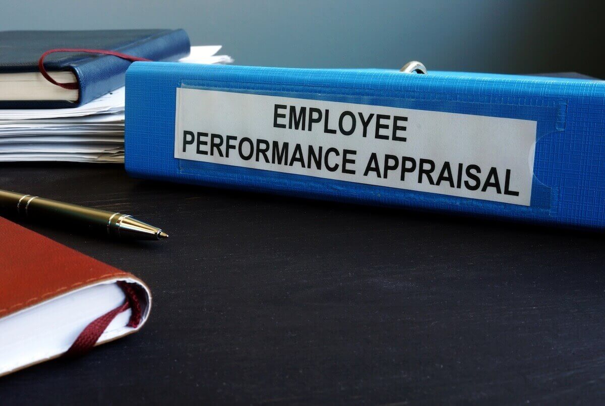 Binder labeled 'employee performance appraisal' on a desk next to a pen and books