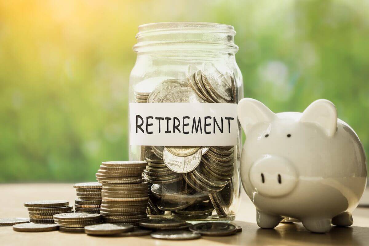 Glass jar labeled 'retirement' with coins in it next to a piggy bank
